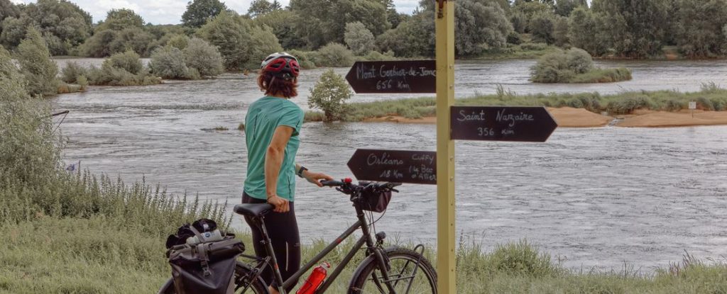 femme à vélo devant la Loire et panneaux de direction